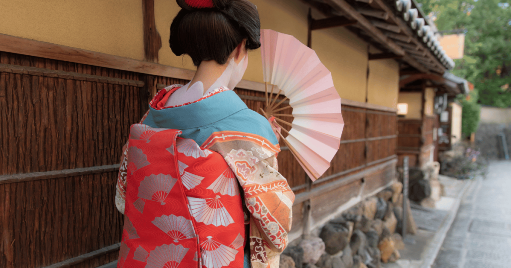 a geisha walks by the side of a macha holding open her fan for protection